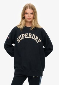 Sort sweatshirt lavet af bomuld, med oversized pasform, rund halsudskæring og "SUPERDAY" logo i cremefarve. Lange ærmer med logodetalje på manchetterne.