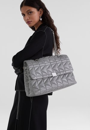 Borsa a tracolla grigia con superficie trapuntata e catena, caratterizzata da una superficie testurizzata e una patta frontale piatta. Accento in metallo argentato nella parte superiore.