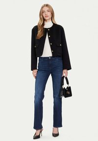 Giacca corta nera con bottoni dorati, dolcevita bianco, jeans blu scuro a gamba dritta, tacchi neri e una piccola borsa nera.