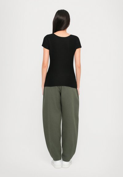Black fitted T-shirt with short sleeves, paired with loose olive green pants and white sneakers; minimalistic design and soft texture.