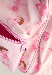 Rosa ryggsäck med ett texturerat tyg som pryds av illustrationer av flickor. Har en dragkedjeficka med en ljusrosa dragkedja och detaljer.