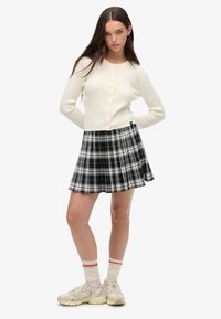 Kremowy sweter z dzianiny zapinany na guziki, połączony z czarno-białą spódnicą w kratę z fałdami. Noszony z kremowymi skarpetkami i beżowymi trampkami.