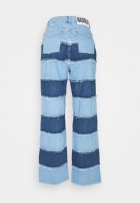 Vaqueros de mezclilla con parches en tonos azul claro y oscuro, de corte acampanado, con bordes deshilachados y un parche con logotipo en la cintura.