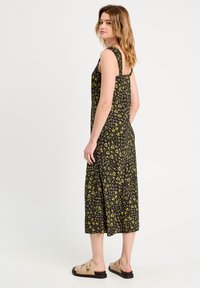 Schwarzes Midikleid mit blühenden Mustern in Gelb, ärmelloses Design und lockere Passform. Kombiniert mit beigen Sandalen mit dekorativen Akzenten.