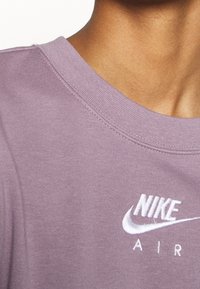 Světle fialové bavlněné tričko s kulatým výstřihem, krátkými rukávy a vyšitým bílým logem "Nike Air" na hrudi. Měkká, texturovaná tkanina.
