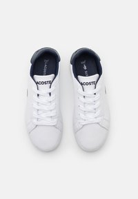White leather sneakers with navy accents, featuring round toes, flat laces, and the "Lacoste" logo. Textured treads for grip.