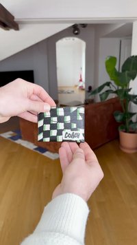 Porta carte a scacchi in bianco e nero con accenti verdi, dotato di molteplici fessure per carte e di un logo "COACH" ben visibile. Materiale in pelle goffrata.