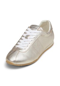 Metallic gold sneaker with white laces, scalloped edging, and perforated detailing. The outsole is tan rubber, highlighting the sleek design.