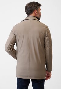 Beige vattentät jacka med rak skärning, som har en hög krage, sömmar och en slät textur. Bakifrån visas minimalistisk detaljering.