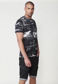 T-shirt u crno-sivom uzorku s japanskim tekstom, kratki rukavi, okrugli izrez, uparen s crnim trapericama do koljena s džepovima.