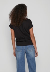 Černé tričko s krátkým rukávem a ohrnutými manžetami, spárované s světle modrými širokými džíny, které mají dvě zadní kapsy a detaily opotřebení.