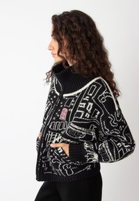 Zwart-witte gebreide cardigan met hoge kraag, gewoven structuur, voorzijde met rits en zijzakken, voorzien van abstracte grafische ontwerpen.