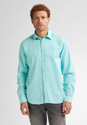 Turquoise langarmshirt van een lichtgewicht stof met een knoopsluiting aan de voorkant en een puntige kraag, gecombineerd met grijze jeans.