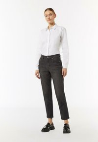 Biała koszula z guzikami zestawiona z ciemnymi dżinsami. Buty są błyszczące, czarne z grubą podeszwą. Prosty design, dopasowana sylwetka, minimalne detale.