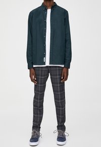 Donker teal knoopshirt, witte crew neck t-shirt eronder, grijs geruite broek en marineblauwe sneakers met lichte zolen.