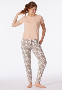 Ljust rosa t-shirt med kort ärm, tillsammans med vita byxor med ett detaljerat blommönster i jordtoner och midja med dragsko.