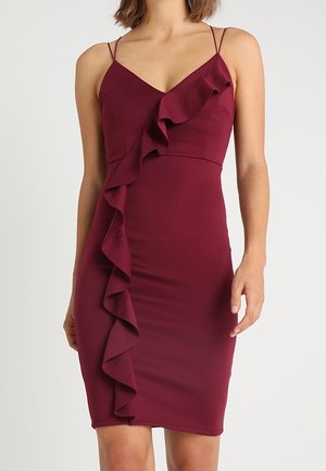 Robe bustier bordeaux avec bretelles spaghetti et un détail de volants sur le côté. Fabriquée en matière stretch, elle présente une silhouette ajustée.