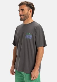 Grijze korte mouwen t-shirt met een cirkelvormig groen en blauw logo op de linkerborst. Relaxte pasvorm en gemaakt van zacht katoen.