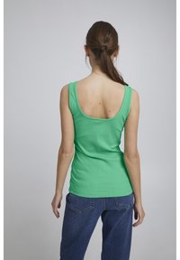 Ribbede grønne tanktop med scoop ryg, tætsiddende design og brede stropper. Matchet med blå denim jeans.
