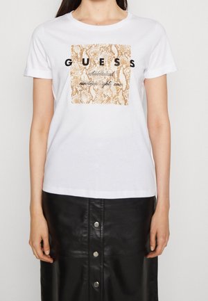 Biała bawełniana koszulka z wzorem skóry węża w kolorze złotym i brązowym, na środku z logo "GUESS" oraz napisem "established nineteen eighty one".