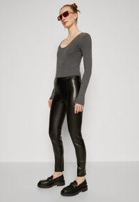 Grey long-sleeve top with a scoop neck, paired with fitted black faux leather pants, and chunky black loafers with a strap detail.