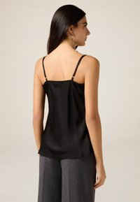 Schwarzes Satin-Camisole mit dünnen verstellbaren Trägern, lockerem Schnitt und glatter Textur, kombiniert mit hoch taillierter grauer Hose.