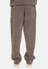 Pantaloni in corduroy color marrone chiaro con vestibilità rilassata, dotati di due tasche laterali e polsini rigati alle caviglie. Texture morbida, design minimal.