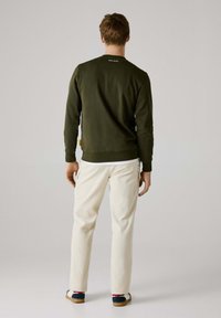 Olijfgroene sweatshirt met geribbelde manchetten en onderkant, met een logo op de achterkant. Gecombineerd met crèmekleurige broek en casual schoenen.