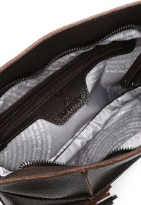 Wnętrze brązowej skórzanej torby na ramię z zamykaną na zamek kieszenią, wyłożone szarym materiałem z nadrukowanym tekstem. Posiada teksturowany materiał i kontrastowy zamek.