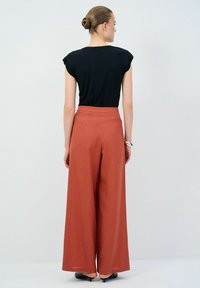 Zwarte top met cap sleeves, gecombineerd met losse, hooggewaiste, roestkleurige broeken. Gladde stofstructuur, wijde pijpen ontwerp en minimalistische stijl.