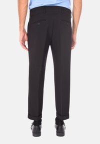 Pantaloni neri eleganti con vestibilità su misura, dotati di due tasche posteriori e una texture liscia. Polsini arrotolati e indossati con scarpe eleganti nere.