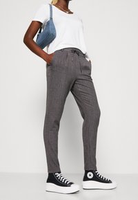 Grå mönstrade byxor med dragsko i midjan, i kombination med en vit t-shirt och svarta högskor. En blå axelväska ingår.