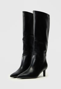 Botas de cuero negro hasta la rodilla con punta afilada y un tacón bajo y delgado. Textura suave con detalles de costura mínimos.
