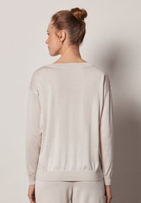 Jasno beżowy sweter z dzianiny o luźnym kroju, z długimi rękawami, ściągaczami na końcach rękawów i szerokim dekoltem, charakteryzujący się gładką, miękką fakturą.