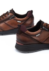 Zapatillas de cuero marrón con un acabado suave, que presentan un cierre de cremallera, un cuello acolchado y una suela de goma con un ligero tacón.