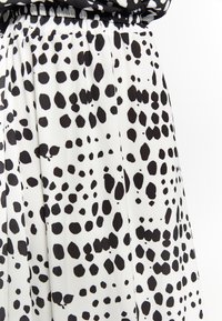 Jupe plissée bicolore noir et blanc avec un motif à pois, fabriquée dans un tissu léger et doux, dotée d'une taille élastique.