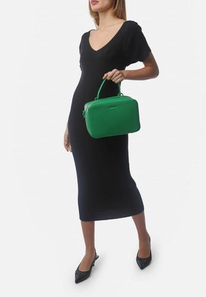 Borsa a tracolla in pelle verde con forma rettangolare, doppi manici superiori e dettagli logo discreti. Indossata insieme a un vestito nero aderente.