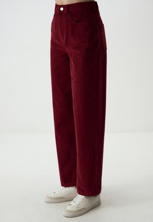 Pantaloni in corduroy bordeaux con design a gamba dritta, dotati di tasche anteriori e chiusura con bottone, abbinati a sneaker bianche.