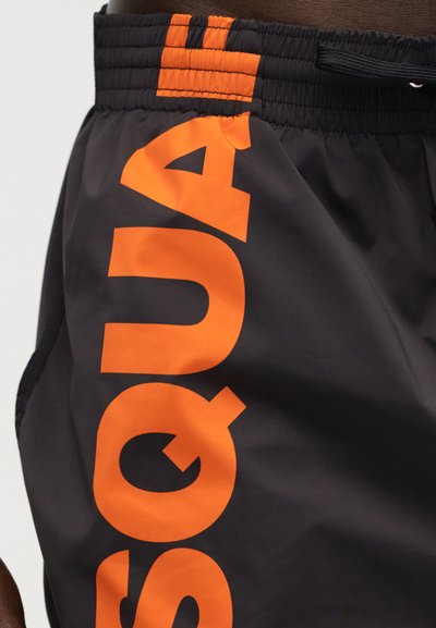 Μαύρα σορτς με φαρδύ πορτοκαλί ελαστικό ζωνάρι και μεγάλα κάθετα πορτοκαλί γράμματα με τη λέξη "SQUAD" στη πλευρά.