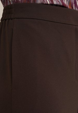 Bruine, gladde broek met een geplooide tailleband en zijnaad. Close-up weergave die de stofafwerking en ontwerpdétails benadrukt.