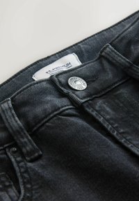 Juodi džinsai iš džinso audinio su metaliniu mygtuko užsegimu ir siuvinėtais akcentais. Etiketėje parašyta „H. Premium Collection“ ir „Next Jeans nuo 1982 m.“