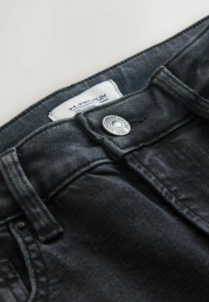 Schwarze Jeans aus Denim mit Metallknopfverschluss und gesteppten Akzenten. Das Etikett trägt die Aufschrift "H. Premium Collection" und "Next Jeans Since 1982."
