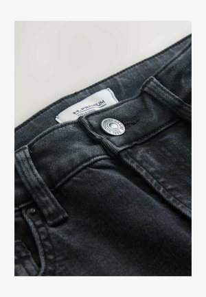 Black denim jeans featuring a metal button closure and stitched accents. Label reads "H. Premium Collection" and "Next Jeans Since 1982."