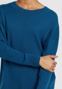 Blauwe gebreide sweater met een ronde hals, geribde manchetten en een licht oversized pasvorm. Zachte textuur met subtiele naaddetails.