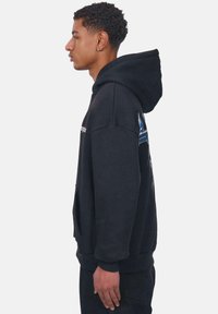 Sort hættetrøje med en stor frontlomme, cropped ærmer og blå grafiske detaljer på siden, udstyret med snore til hætten.