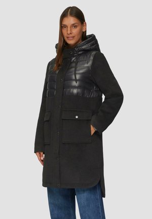 Manteau noir avec un panneau matelassé noir brillant et épais sur la poitrine et la capuche. Dispose de deux poches avant et d'une fermeture à bouton.