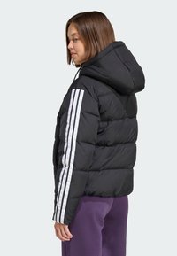 Chaqueta negra tipo plumón con capucha, costuras horizontales y rayas blancas verticales a lo largo de las mangas. El material parece liso y brillante.