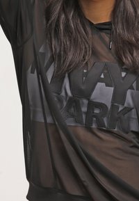 Sudadera negra, transparente y de corte oversized con "IVY PARK" en letras negritas negras y un tejido suave, que presenta un ajuste relajado y capucha con cordón.