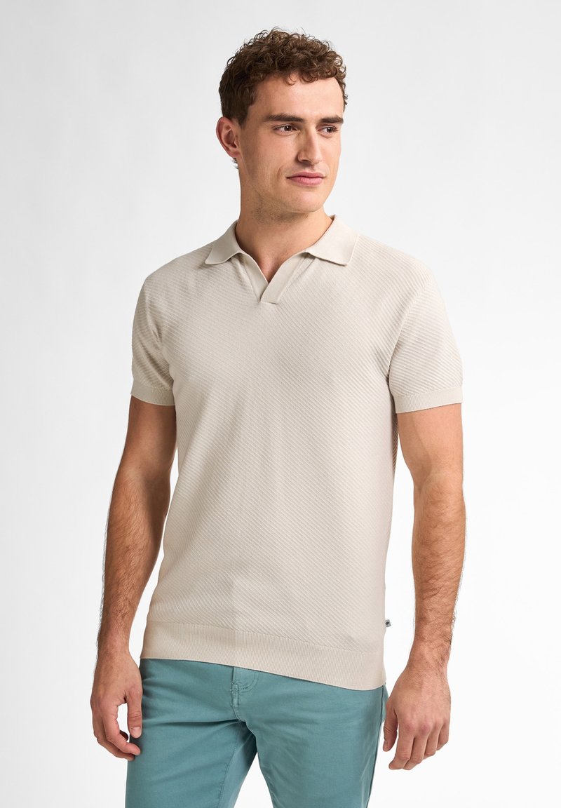 Beige strikket polo t-shirt med ribbede detaljer, korte ærmer og v-udskæring, parret med lyse teal bukser.