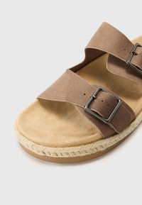 Sandale en suede brun avec deux larges lanières et boucles en argent, dotée d'une semelle intérieure douce et d'une semelle en jute.